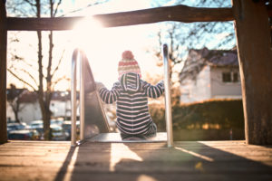 Kleines Kind auf einer Rutsche im Sonnenlicht, von hinten Kleines Kind auf einer Rutsche im Sonnenlicht, von hinten